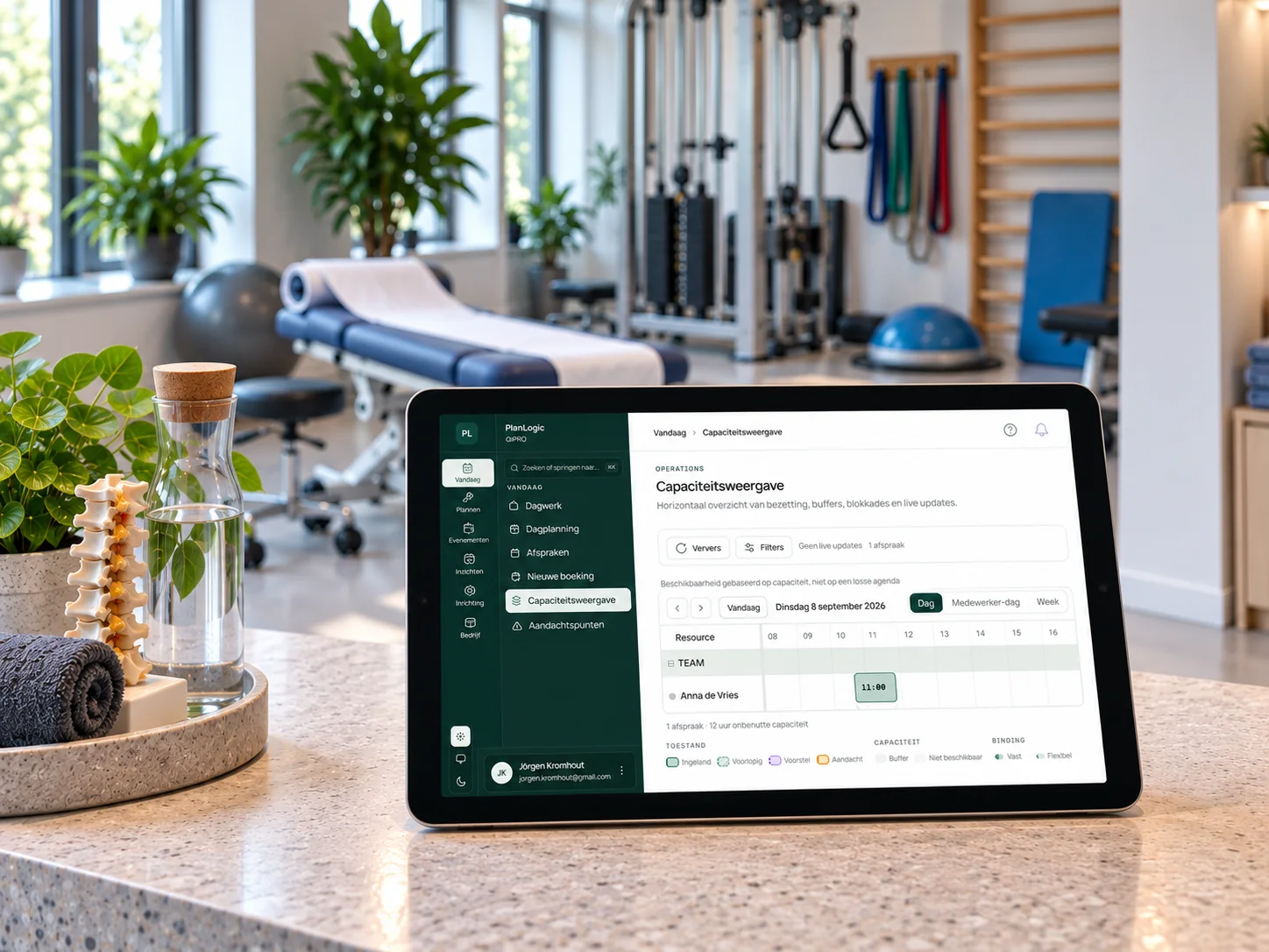 Balie van een fysiotherapiepraktijk met de capaciteitsweergave van PlanLogic op een tablet, behandeltafel en toestellen op de achtergrond