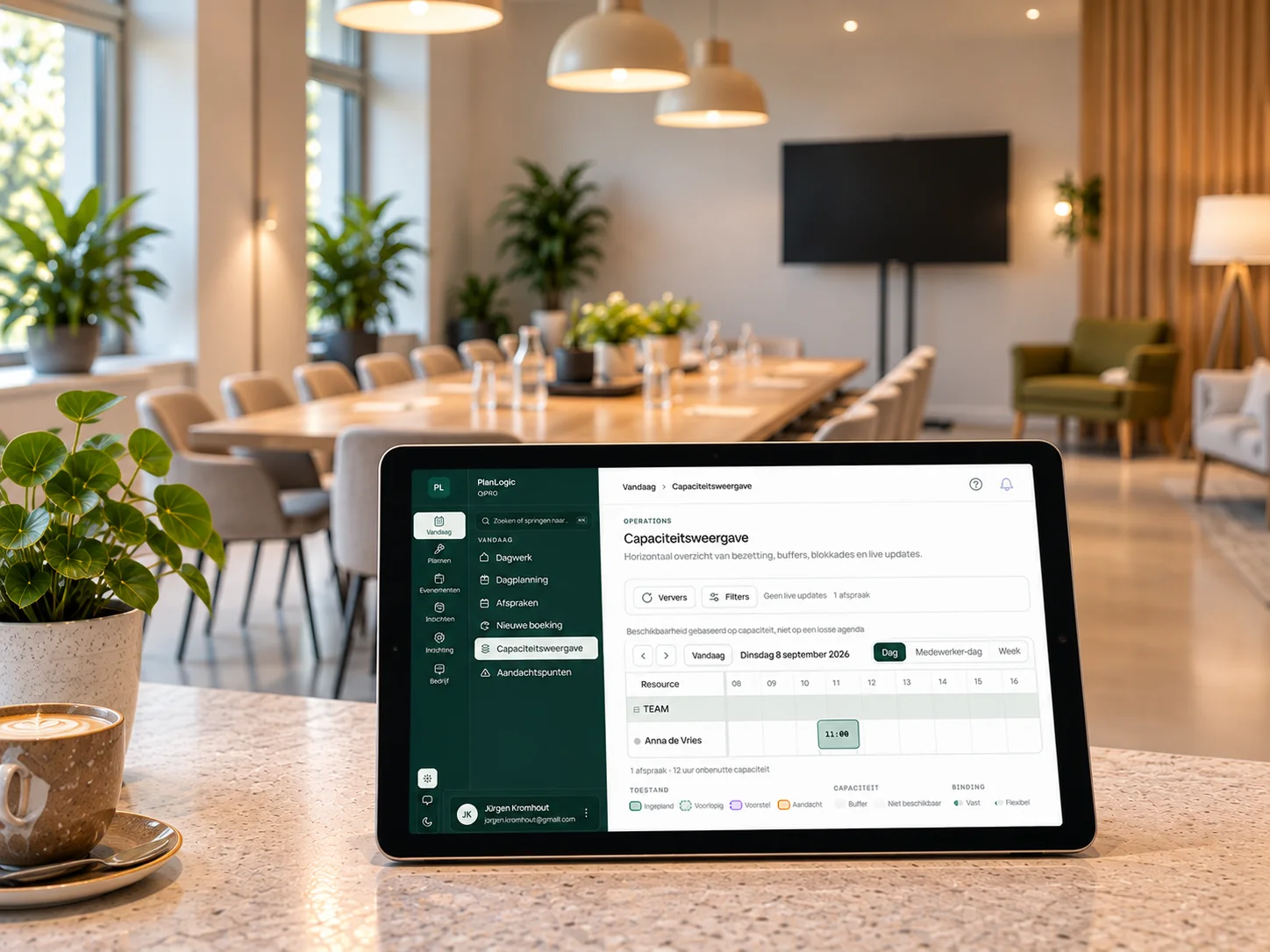 Balie van een vergaderlocatie met de capaciteitsweergave van PlanLogic op een tablet, boardroom-opstelling en scherm op de achtergrond