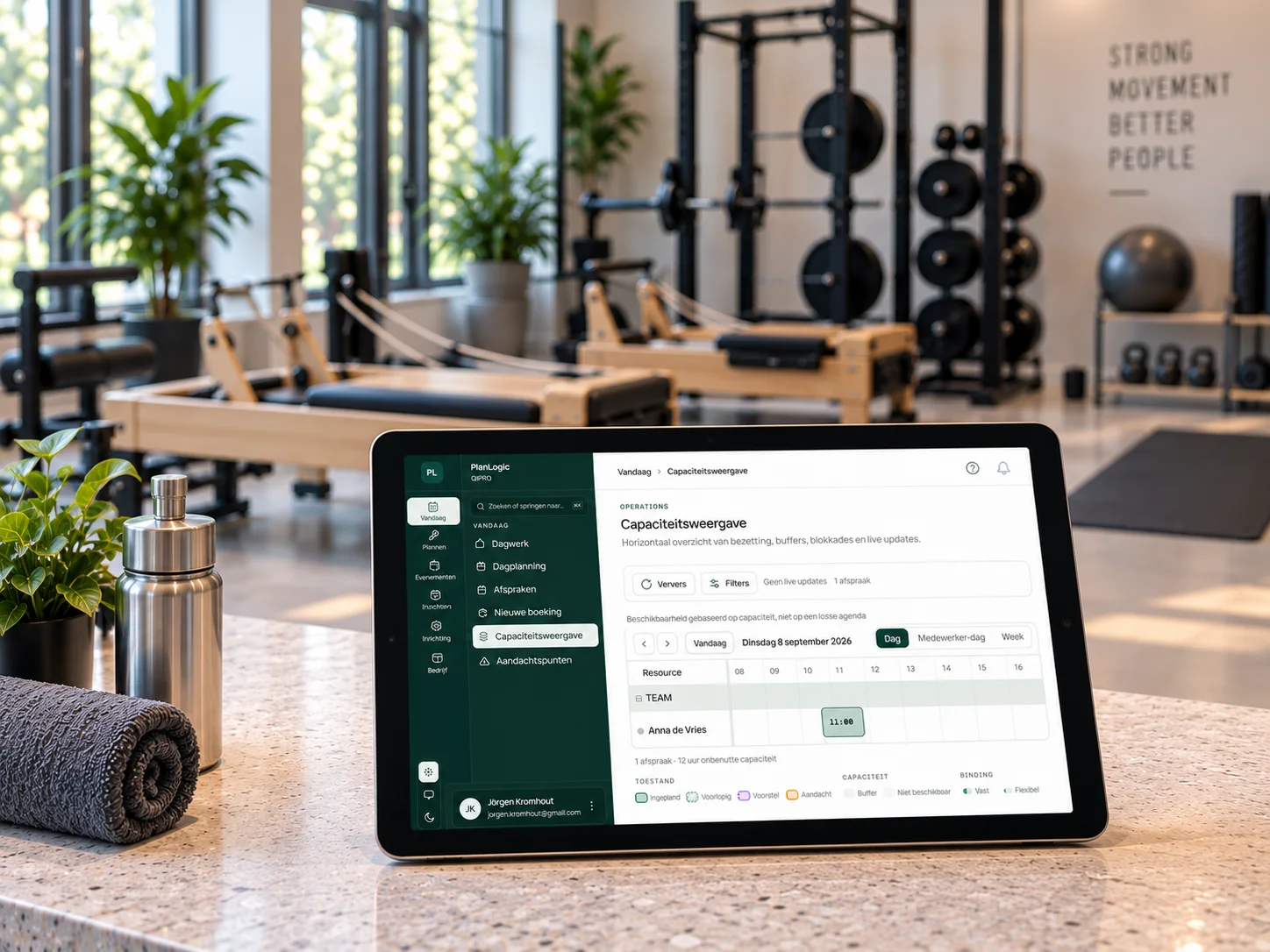 Balie van een trainingsstudio met de capaciteitsweergave van PlanLogic op een tablet, reformers en rack op de achtergrond